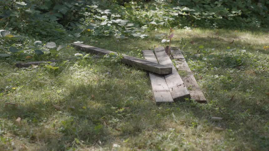 A wooden beam being dropped onto a pile of wood lying on top of the grass