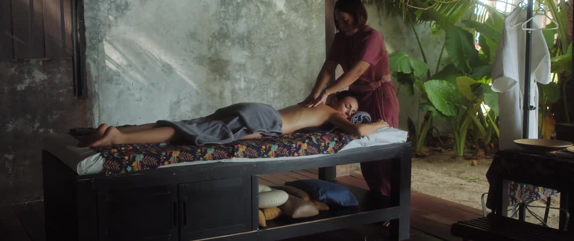 A masseuse massages the back of a woman resting on a massage table during the day