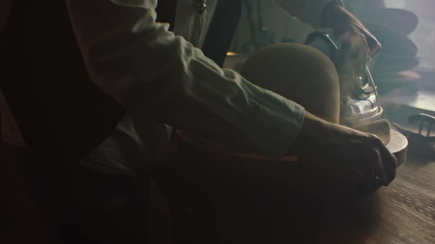 Hands of a male hatter in a workshop indoors ironing the brim of a hat during day time