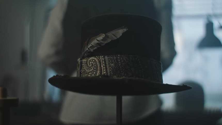 Closeup of a hat with details and feathers with a man working in hat manufacturing services in the background