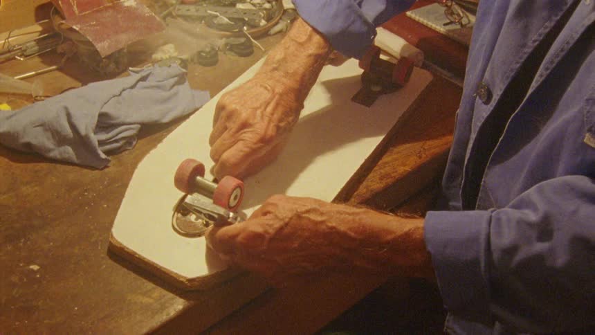 Old man working on a skateboard in a workshop at night