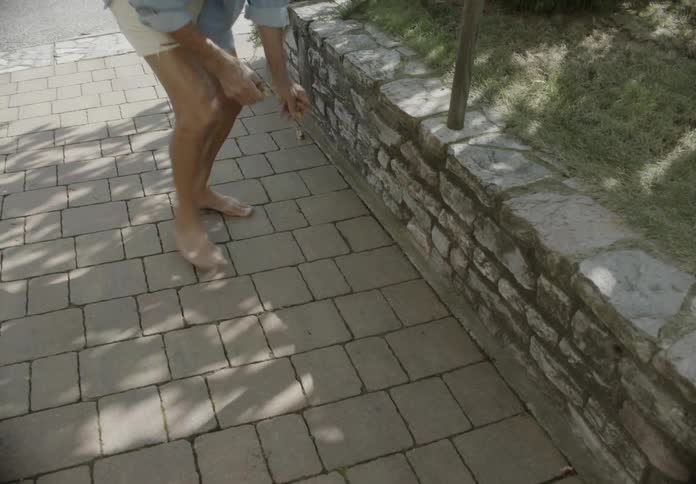 Elderly man outdoors picking up leaves from the floor next to the road and other houses on the neighborhood during day time