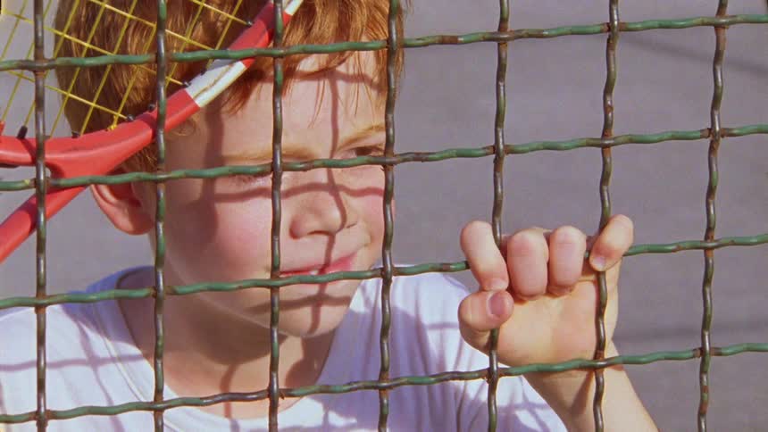Closeup of a child with hand resting on the railing and holding a racket celebrating happily
