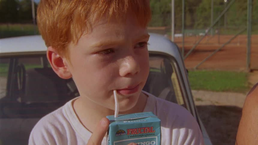 A redhaired boy is drinking something from a package using a straw