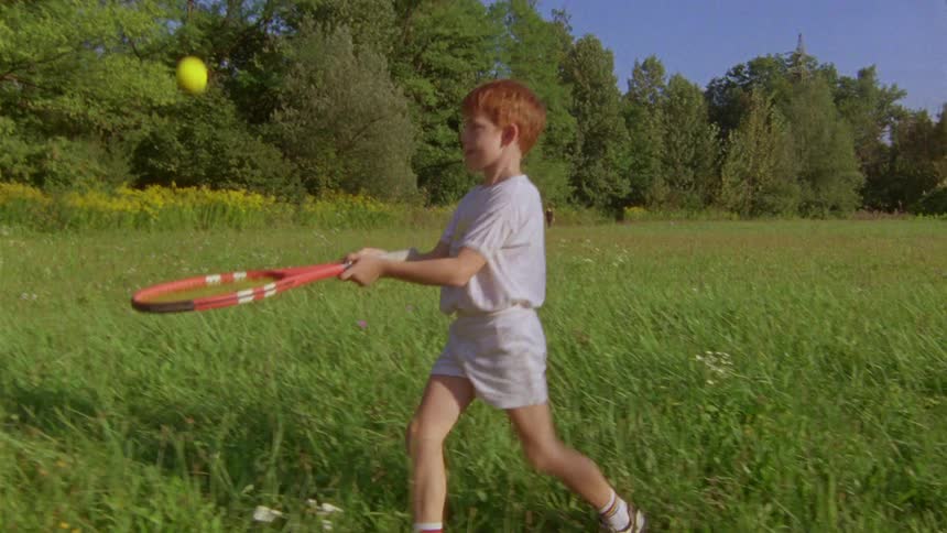A boy playing on the lawn with a racket and tennis ball