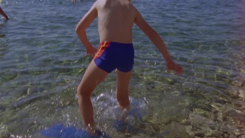 A boy wearing flippers wades through the shallow ocean water