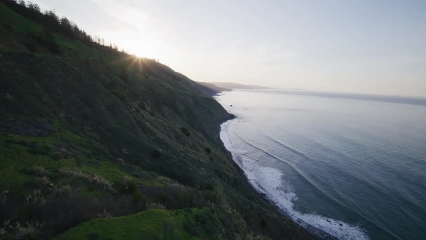 Aerial of the Pacific coastline with the sun rising behind the mountain