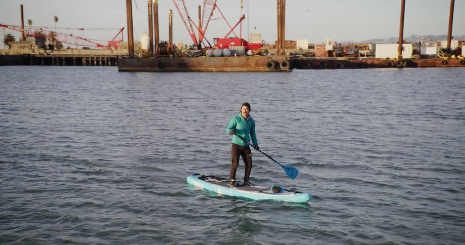 Man on a paddle board on the San Francisco Bay with undustrial barges