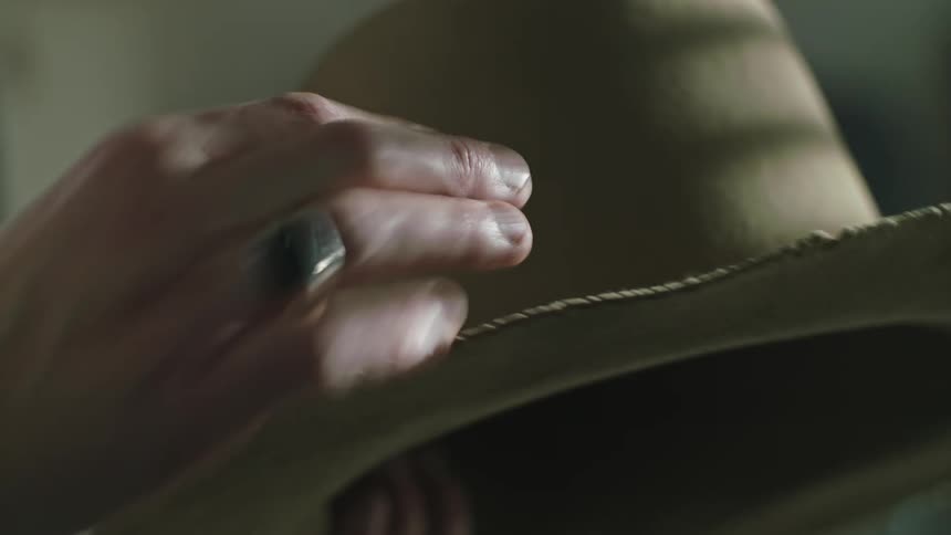 Close up of a mans hand rubbing the brim of a cowboy hat with light shing on his hand