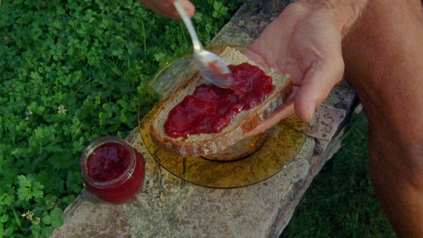 A person spreading jam on toast outdoors