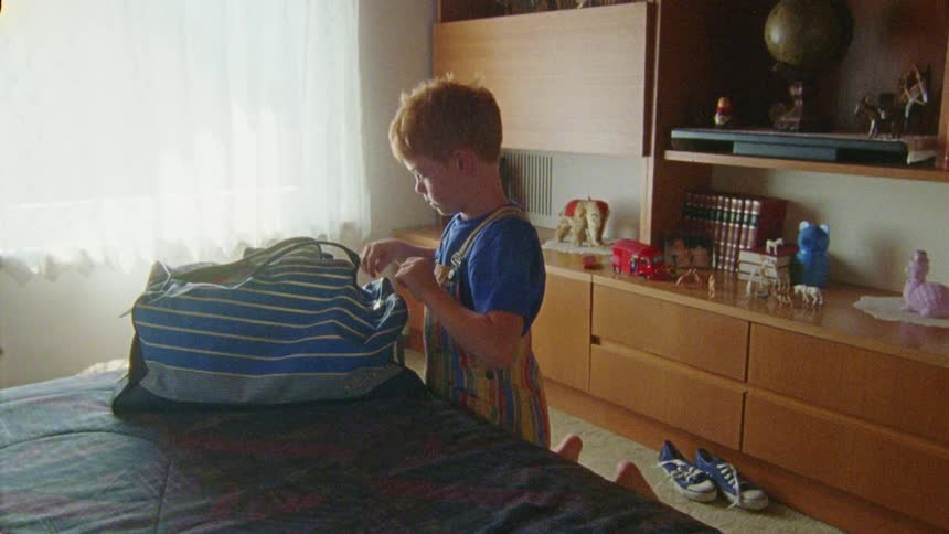 A child packs a bag and walks out of the bedroom
