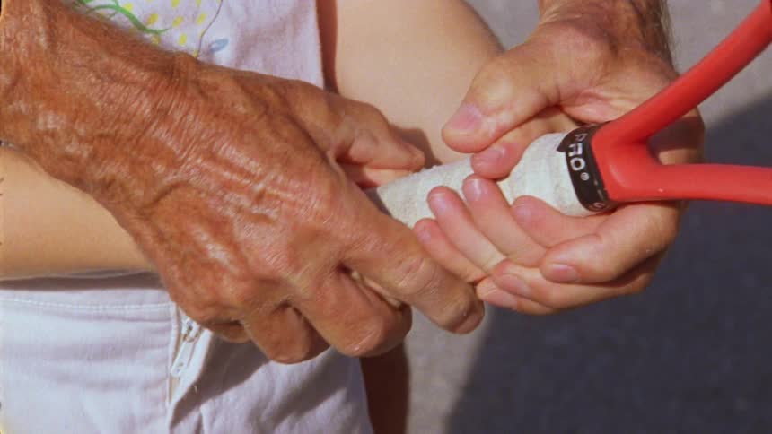 Closeup of hands of an elderly person holding hands with a child and teaching them how to throw with a tennis racket