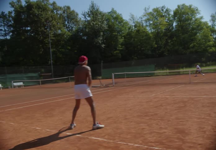 A pair of men play tennis on a dirt tennis court