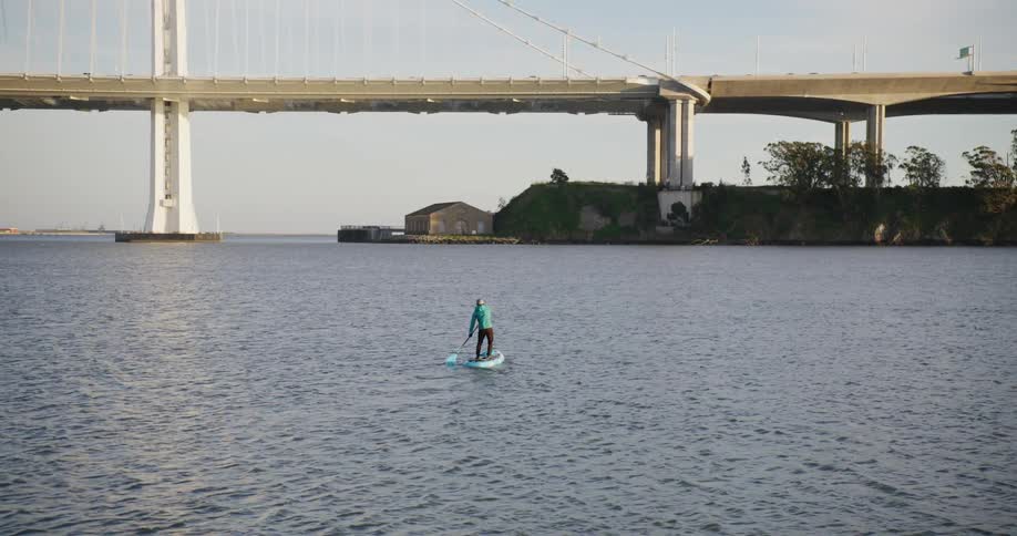 A man standing on a paddle board near the San Francisco Oakland Bay Bridge