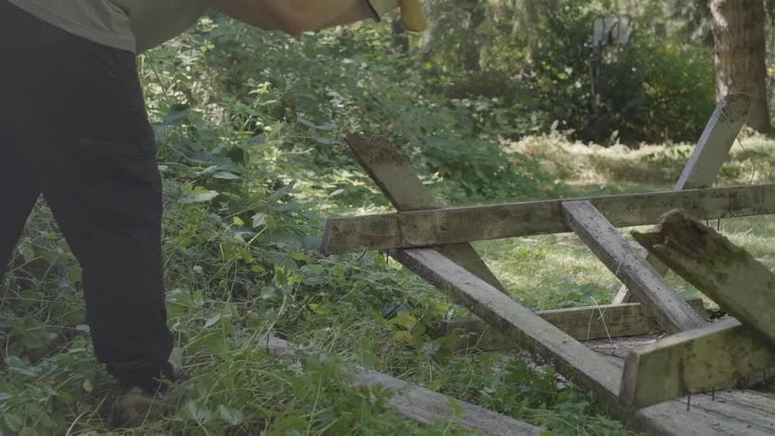 Man demolishes old wooden picnic table in yard with an ax