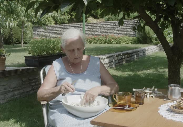 Elderly woman sitting in a chair in the garden peeling a food item