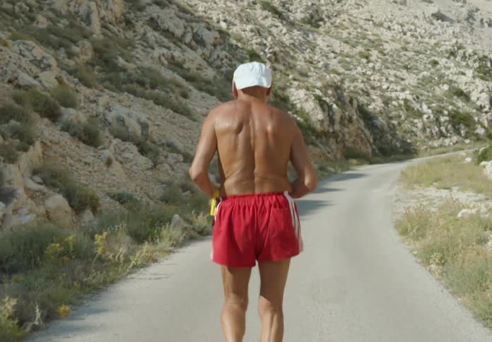 An elderly man running shirtless on a mountain path