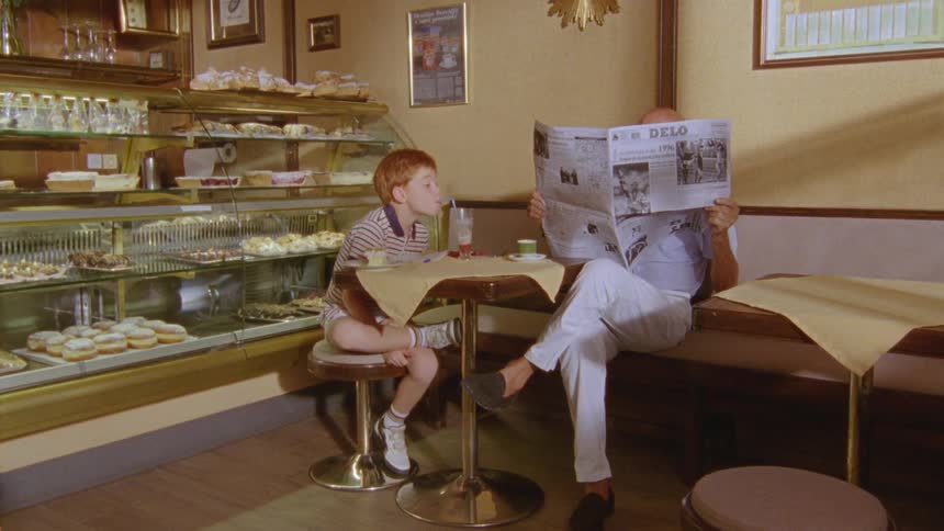 A boy is drinking juice at a table in a bakery