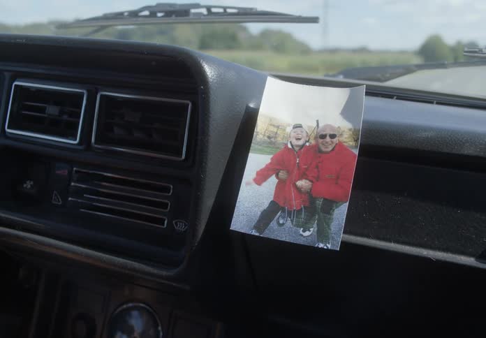 A photograph of a boy and bald man lies on cars dashboard