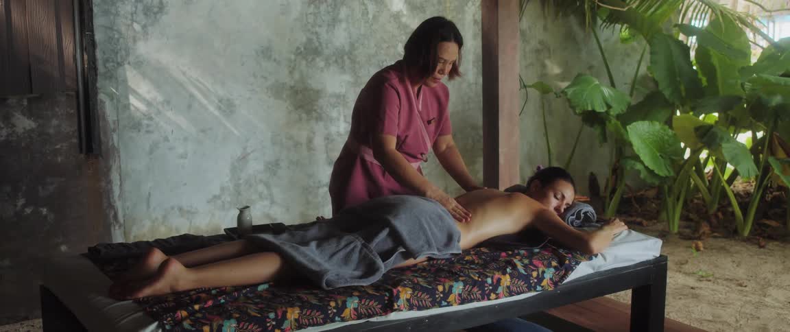 A woman giving a hand massage to a woman who is lying on a bed