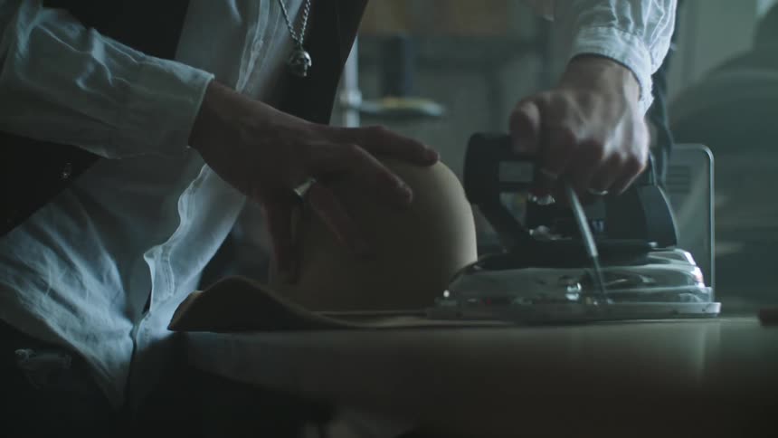 Tailor with white shirt and black vest and skull necklace irons sun hat