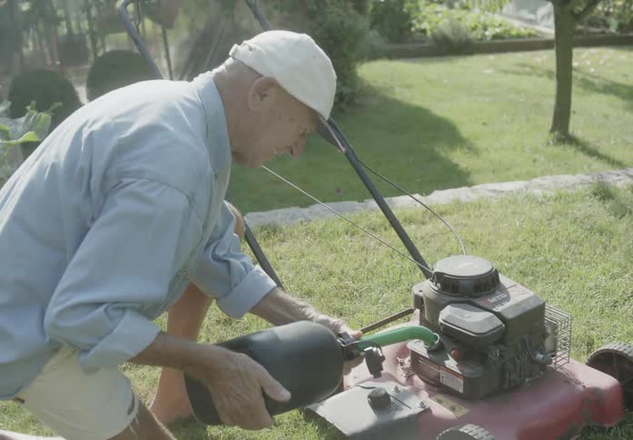 A man fueling his lawnmower with gasoline from a gallon