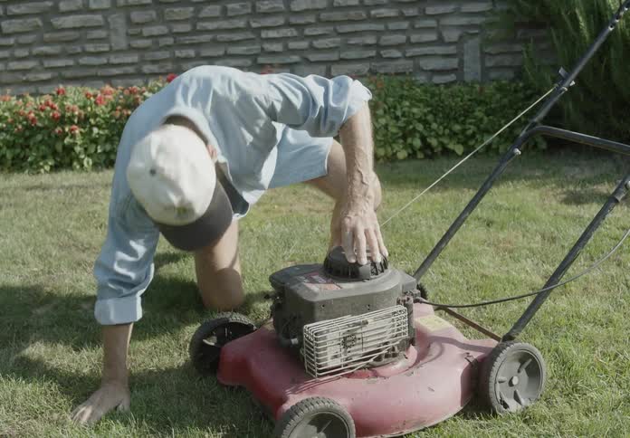 An older man is inspecting and attempting to start a lawn mower