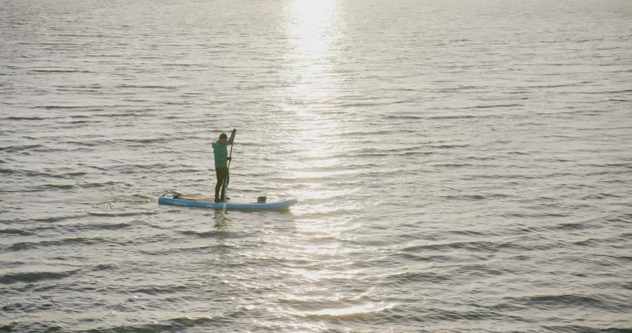 A man paddles on a stand up board in the San Francisco Bay at sunset