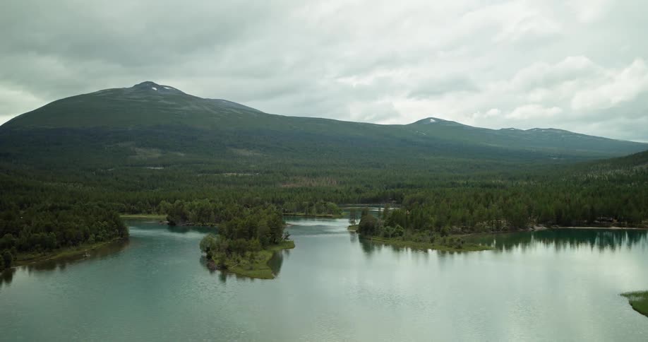 A calm lake with trees scattered around it and mountains in the background
