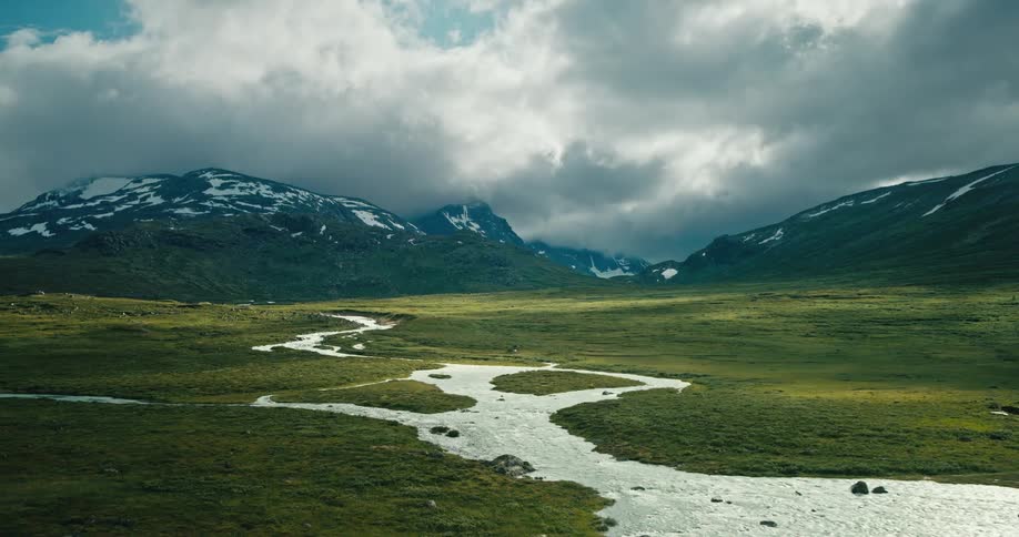 In spring a vast plain field with a river guiding the way toward a mountain its peak adorned with lingering patches of snow
