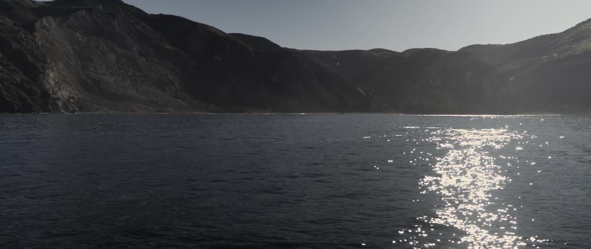 The sun is reflecting on the water by this mountain range