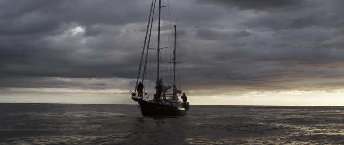 A large boat has it's sails down at sunset