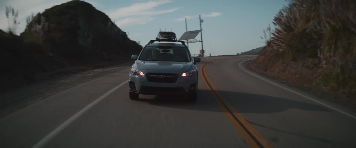 A vehicle with surfboards on its roof rack drives a long a curved road