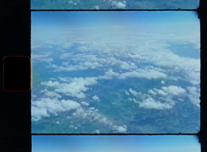 An aerial view above the clouds over fields of hilly landscape with mountains and green valleys while flying with a plane over a rural and less populated countryside in Europe on retro Super-8 film