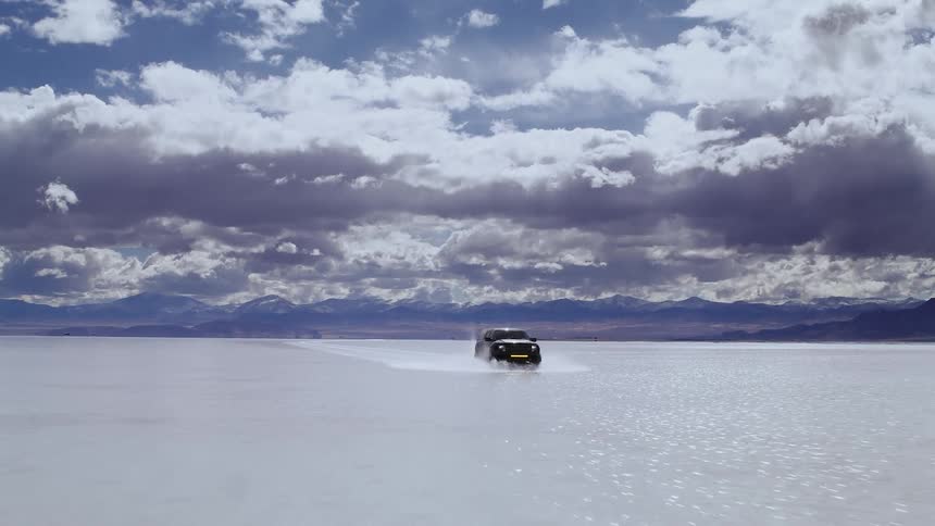 A truck racing across flooded salt flats with a gradual camera lift, cinema drone footage