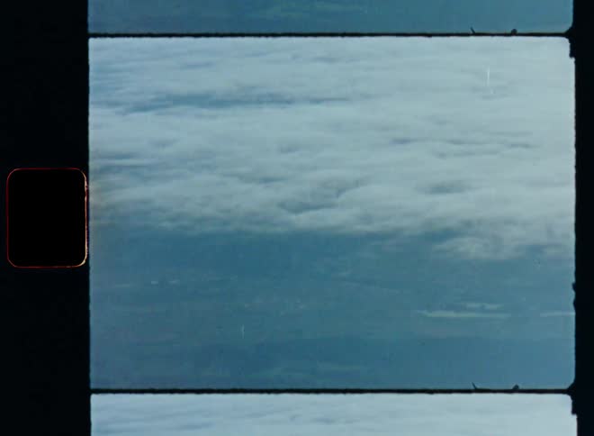 Aerial Super 8 footage looking down onto a cloud cover or layer of clouds in the sky over a natural landscape with green farm fields and forests while flying above the clouds