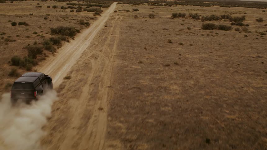 A truck racing through the desert on a dirt road, fast aerial footage