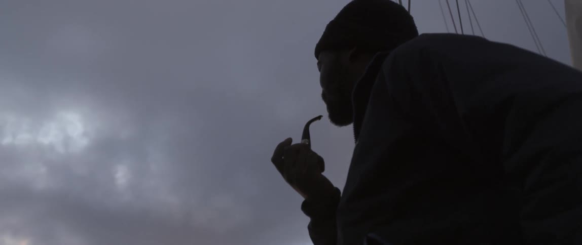 A man is smoking from a pipe with heavy clouds above