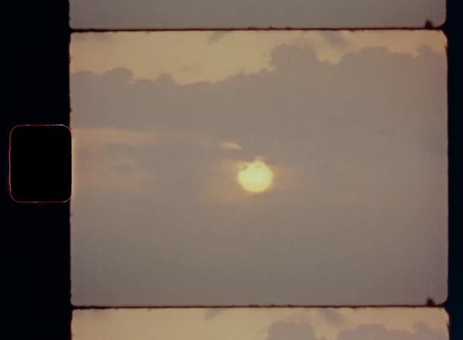 Super 8mm tele shot with handheld shaky movement of the golden or orange sun shining through clouds during the evening of a cloudy day as the sunshine breaks thru and a seagull bird flies by during romantic sunset over the sea