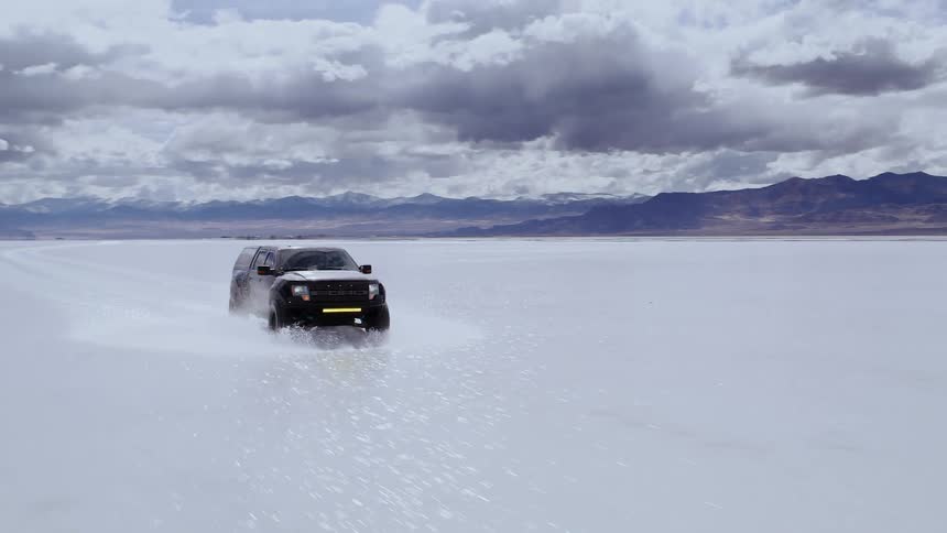 A truck driving across the flooded salt flats in Utah, high speed aerial footage