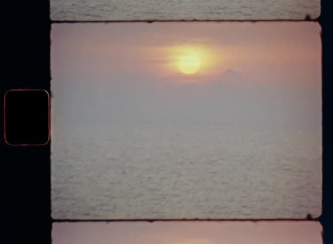 Glowing romantic sunset over the ocean on a gloomy overcast day as the sun breaks through the clouds at the horizon with reflections and light on the rippling surface with upward tilting hand-held camera movement during golden hour