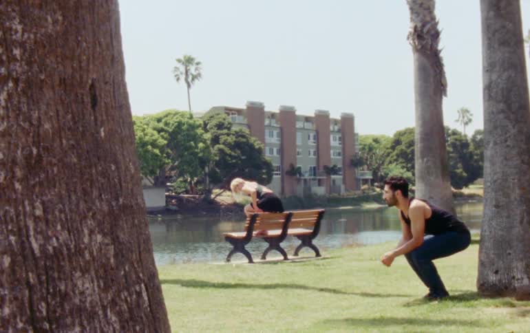 A man standing against a tree and a woman on a bench before they both start dancing around