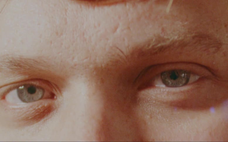 A man looks directly at the camera before diverting his eyes elsewhere