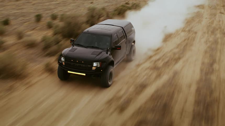 A truck racing through the desert on a dirt road, high speed drone footage