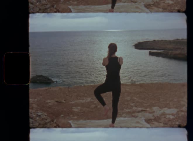 Moving towards a woman practicing yoga on a cliff or the beach by the sea on a cloudy day doing the mountain or tree position pose to improve balance and mind body connection as the sun shines through the clouds in the evening of a warm summer day
