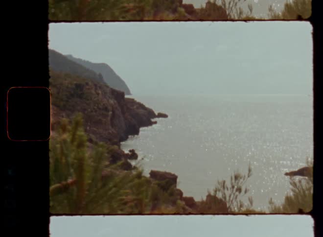 A stunning view of the sea or ocean horizon from a mountain peak next to the coast or beach on a warm and mild spring or summertime day with green pine trees and bushes growing on the stones and rocky cliffs of the spectacular coastline