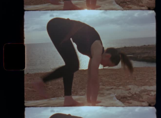Silhouette of sportive woman doing a yoga flow with different poses including the downward facing dog pose on blanket laying on the rocks next to the ocean at sunset with backlight and epic clouds above the horizon over water with sun shine reflections