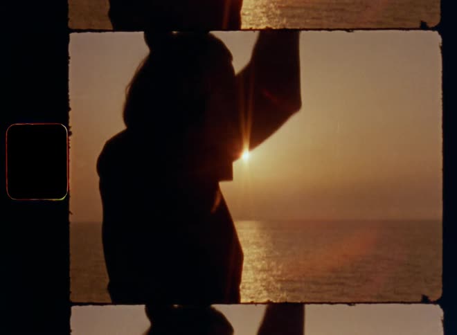 Dark silhouette of young man against the bright glowing evening sky during sunset in front of the shining sun while doing yoga at the beach raises arms and places hands together to meditate or pray with inner peace and harmony on nostalgic vibe 8mm film