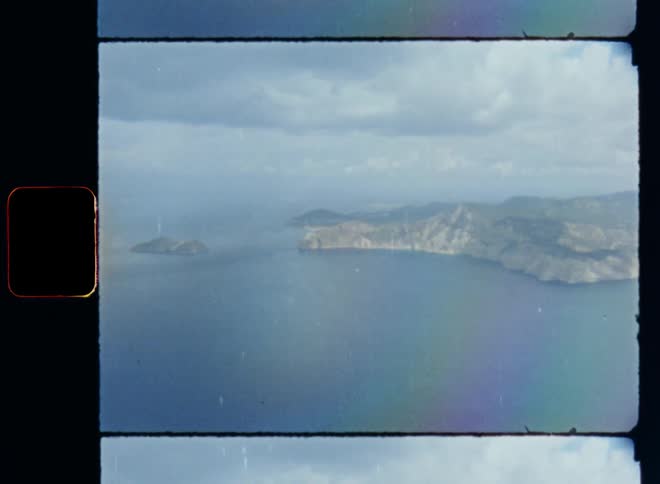 Aerial view of small islands with hills and coast located beneath a cloudy sky from a passenger seat out of the window of an aircraft or plane while approaching the destination in the middle of nowhere or the ocean on a cloudy day with sun shining