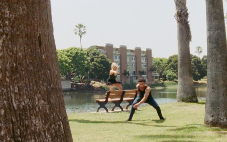 A man and a woman in the park dancing on a bench close to a lake